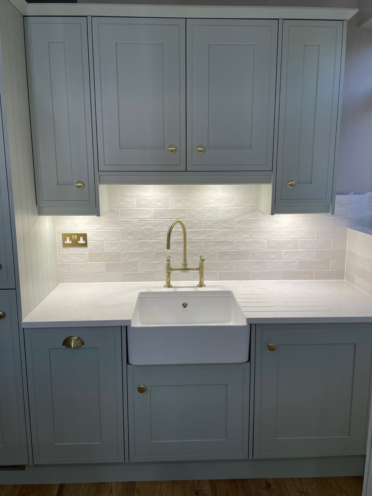 Grey green shaker cabinets around a ceramic sink with a brass tap