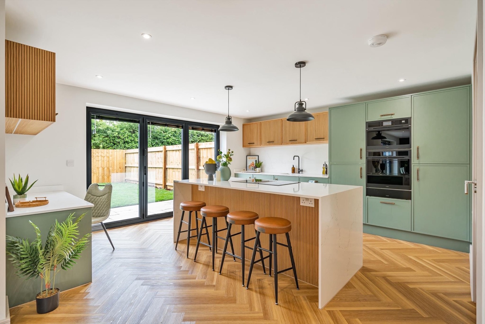 Sage green kitchen with a fluted oak island and leather bar stools